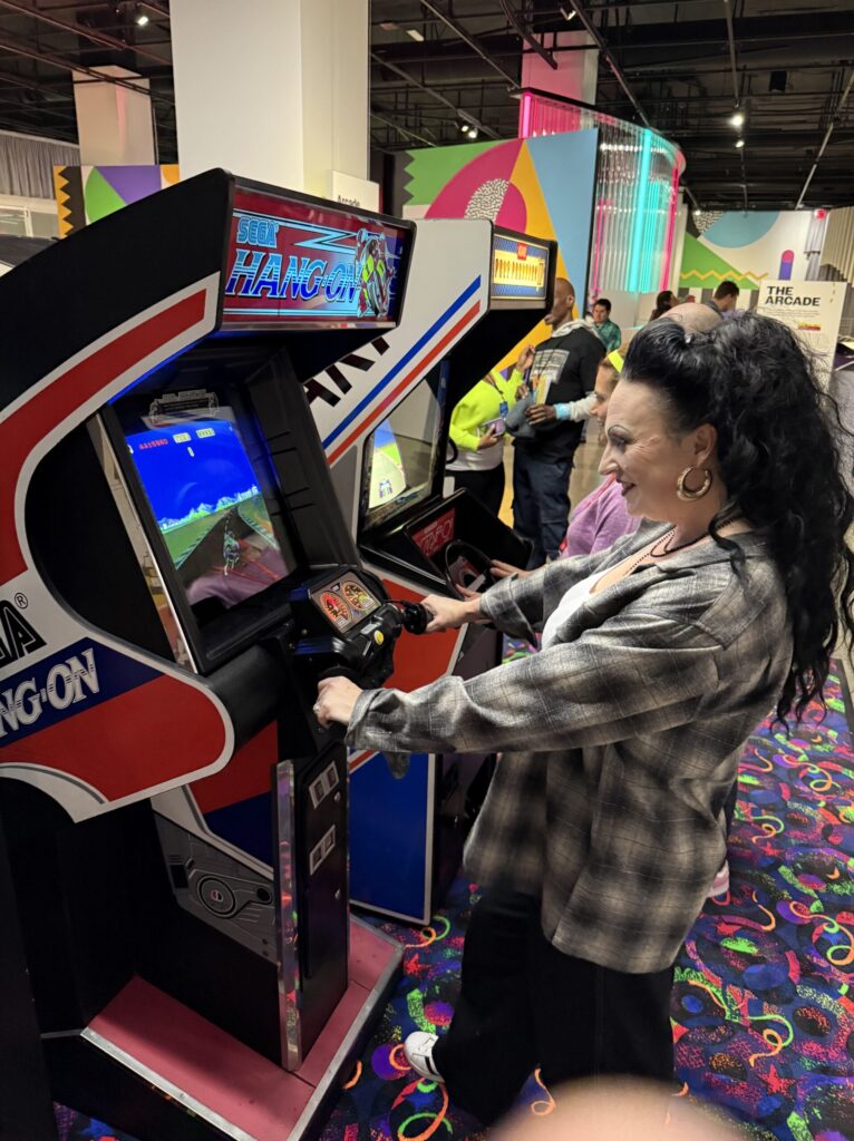 Regina Luz Jordan founder of the Hollywoodland News playing Hang-On arcade motorcycle racing game released by Sega in 1985 . This arcade is on exhibit and playable at the Totally Awesome Exhibit at the Petersen Automotive Museum. Photograph by Mark Jordan for Hollywoodland News